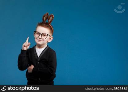 Happy Easter kids. child boy in rabbit bunny ears on head with glasses on blue studio background. Pointing up. Looking and smiling at camera. Happy Easter kids. child boy in rabbit bunny ears on head with glasses on blue studio background. Pointing up. Looking and smiling at camera.