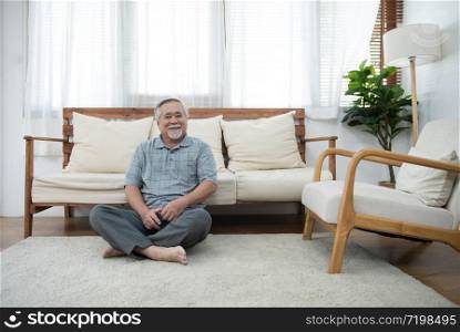 Happy elder senior man in casual sit on carpet lean on sofa look at camera in living room at home.