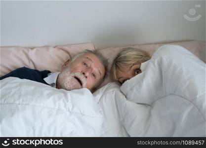 happy elderly couple caucasian senior man and woman resting together in white blanket in bedroom, retirement love lifestyle concept