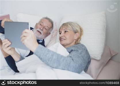 happy elderly couple caucasian senior man conferrencing with family by using on tablet in white blanket in bedroom, retirement love family lifestyle concept