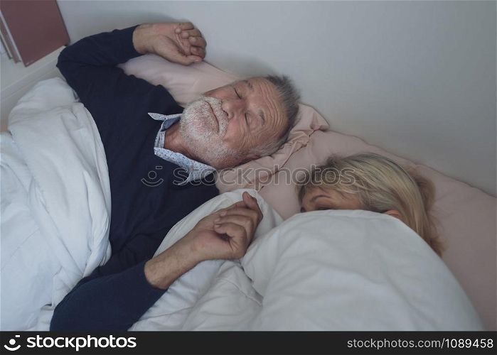 happy elderly couple caucasian senior man snoring and woman sleeping together in white blanket in bedroom, retirement love lifestyle concept