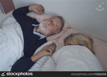 happy elderly couple caucasian senior man snoring and woman sleeping together in white blanket in bedroom, retirement love lifestyle concept
