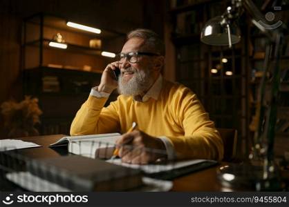 Happy elderly man laughing and talking mobile phone while working at home office in evening. Happy elderly man talking phone while working at home office in evening