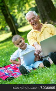 happy elderly senior grandfather and child in park using laptop computer