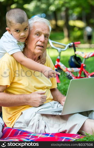 happy elderly senior grandfather and child in park using laptop computer