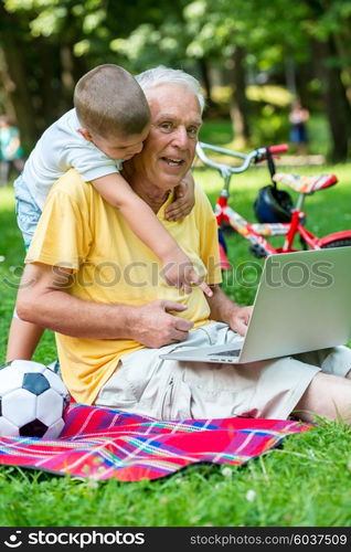 happy elderly senior grandfather and child in park using laptop computer