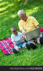 happy elderly senior grandfather and child in park using laptop computer