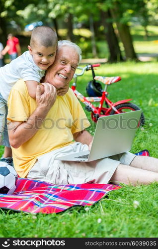 happy elderly senior grandfather and child in park using laptop computer