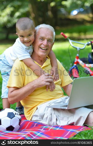 happy elderly senior grandfather and child in park using laptop computer