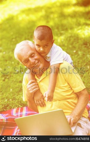 happy elderly senior grandfather and child in park using laptop computer. grandfather and child using laptop