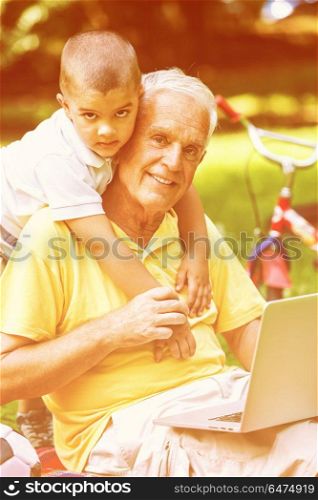 happy elderly senior grandfather and child in park using laptop computer. grandfather and child using laptop