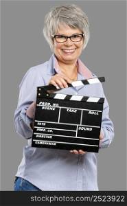 Happy elderly woman holding a clapboard, isolated on a gray background
