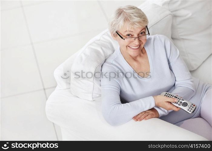 Happy elderly woman on a white sofa with a remote control on TV