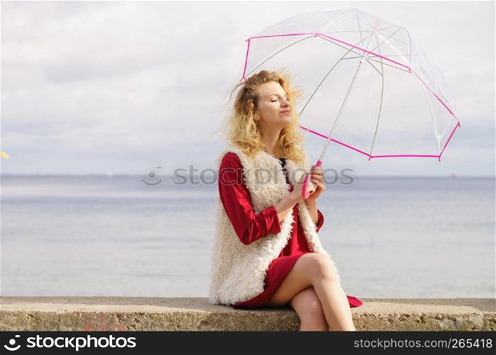 Happy elegant adult woman holding transparent umbrella against sky. Weather forecasting concept.. Happy woman holding umbrella