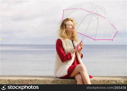Happy elegant adult woman holding transparent umbrella against sky. Weather forecasting concept.. Happy woman holding umbrella