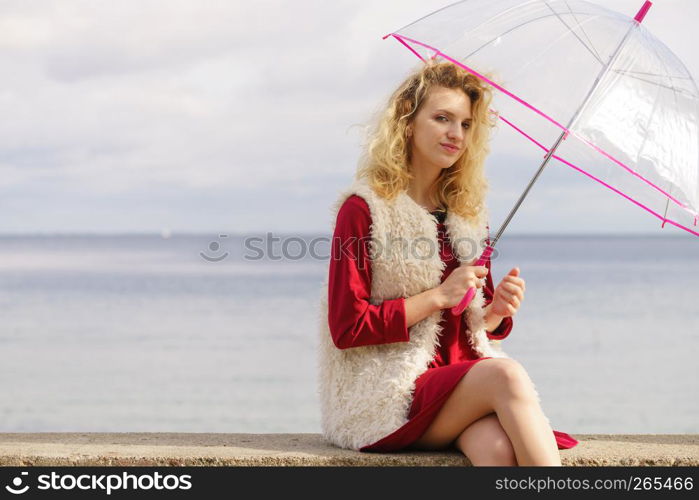 Happy elegant adult woman holding transparent umbrella against sky. Weather forecasting concept.. Happy woman holding umbrella