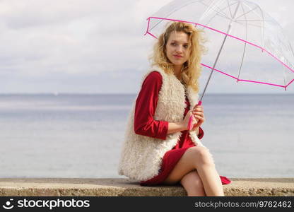 Happy elegant adult woman holding transparent umbrella against sky. Weather forecasting concept.. Happy woman holding umbrella