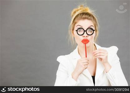 Happy elegant woman holding carnival accessoies on stick having fun at work wearing white office jacket. Happy elegant woman holding carnival accessoies on stick