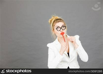 Happy elegant woman holding carnival accessoies on stick having fun at work wearing white office jacket. Happy elegant woman holding carnival accessoies on stick
