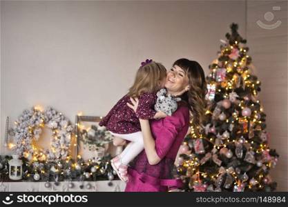 Happy embrace of mother and daughter against the background of the Christmas tree.. Mama throws up a small daughter on hands 9582.