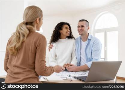 happy embraced couple conversing with female realtor