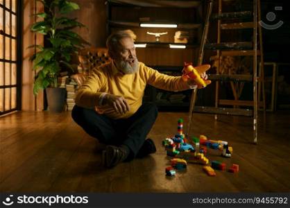 Happy enthusiastic old retired man playing toys while sitting on home floor over cozy eco-friendly interior design. Happy enthusiastic old retired man playing toys while sitting on home floor