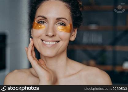 Happy european girl doing spa procedures and touches her face skin. Face of young woman which applies collagen eye patches. Relaxation and skincare. Golden anti age and anti wrinkle patches.. Happy european girl doing spa procedures and touches her face skin. Relaxation and skincare.