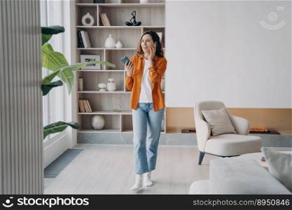 Happy european girl has phone call at home. Pretty young woman is using airpods. Wireless earphones. Technology using, leisure and communication concept. Beautiful modern interior.. Happy european girl has phone call at home. Pretty young woman is using airpods.