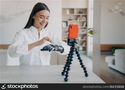 Happy european handicapped woman is filming on phone camera. Amputee is taking video how to use robotic cyber arm. Pretty disabled girl is blogger. Rehabilitation and wellbeing concept.. Happy european handicapped woman is filming on phone camera. Disabled girl is blogger.