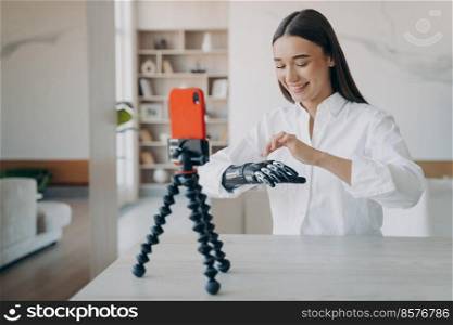 Happy european handicapped woman is filming on phone camera. Amputee is taking video how to use robotic cyber arm. Pretty disabled girl is blogger. Rehabilitation and wellbeing concept.. Happy european handicapped woman is filming on phone camera. Disabled girl is blogger.