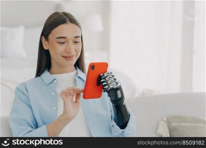 Happy european woman is chatting on smartphone. Girl is holding the phone with bionic artificial arm. Attractive caucasian woman at home. Innovation and science development concept.. Happy european woman with bionic artificial arm chatting on smartphone. Innovation development.