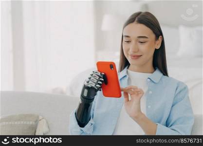 Happy european woman is chatting on smartphone. Girl is holding the phone with bionic artificial arm. Attractive caucasian woman at home. Innovation and science development concept.. Happy european woman with bionic artificial arm chatting on smartphone. Innovation development.