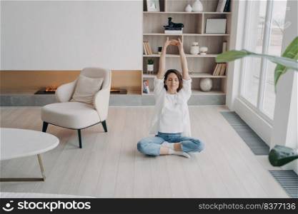 Happy european woman is meditating with her eyes closed. Girl is doing stretching exercises on floor at home. Lady sitting in lotus asana. Morning gymnastics. Concentration and balance concept.. Girl is doing stretching exercises on floor at home. Happy woman is meditating with her eyes closed.