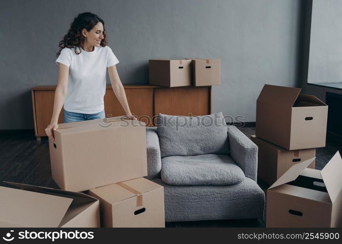 Happy european woman relocates alone. Proud single lady in casual outfit moves. Cardboard boxes on floor. Real estate purchase and mortgage. Delivery service ordering for the boxes unloading.. Proud single european lady in casual outfit moves. Cardboard boxes on floor. Real estate purchase.