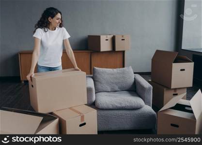 Happy european woman relocates alone. Proud single lady in casual outfit moves. Cardboard boxes on floor. Real estate purchase and mortgage. Delivery service ordering for the boxes unloading.. Proud single european lady in casual outfit moves. Cardboard boxes on floor. Real estate purchase.