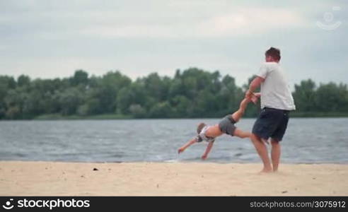 Happy excited father and son playing on summer beach. Father spinning his cute little boy around and giving him piggyback ride on the beach