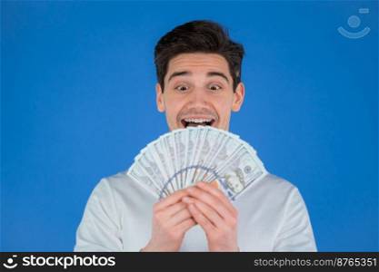Happy excited man with cash money - USD currency dollars banknotes on blue wall. Symbol of jackpot, gain, victory, winning the lottery. High quality photo. Happy excited man with cash money - USD currency dollars banknotes on blue wall. Symbol of jackpot, gain, victory, winning the lottery