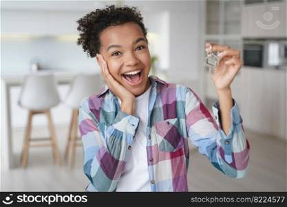 Happy excited mixed race teen girl showing keys to modern studio apartment, looking at camera indoors. Overjoyed lucky young teen lady holds key to flat. Relocation to new home, real estate rental.. Happy excited mixed race young girl showing keys to modern studio apartment. Relocation to new home