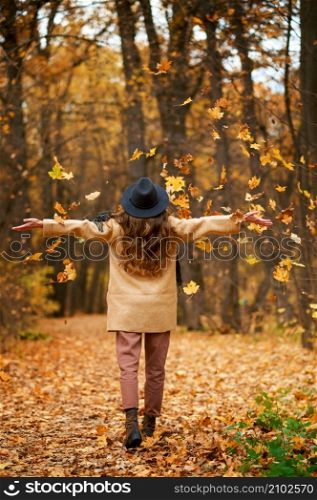 Happy excited young woman under leaves fall. View from back. Tranquility and relax in fall season. Happy excited young woman under leaves fall