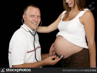 Happy expectant father listening to his wife&rsquo;s pregnant belly with a stethoscope.