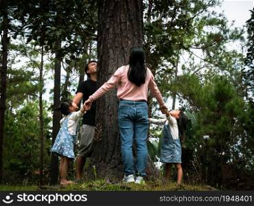 Happy families stand holding each other&rsquo;s hands around a large tree. Happy family playing outdoors. Environmental conservation concept.