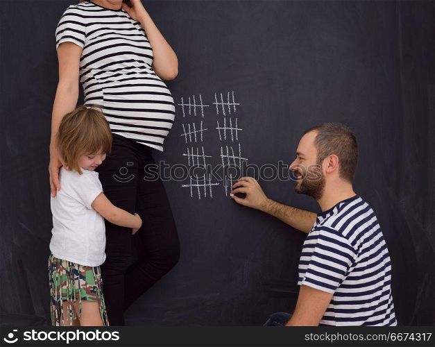 happy family accounts week of pregnancy. young pregnant couple with cute little daughter accounts week of pregnancy and writing them with chalk on blackboard