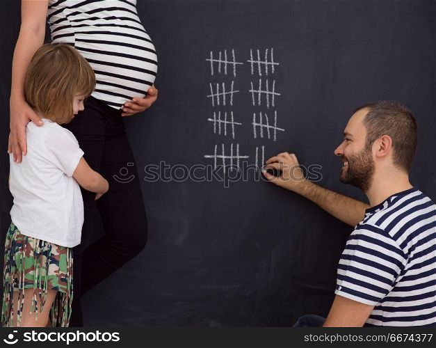 happy family accounts week of pregnancy. young pregnant couple with cute little daughter accounts week of pregnancy and writing them with chalk on blackboard