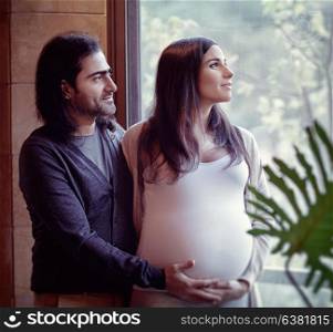 Happy family at home, husband with his cute pregnant wife looking in the window, with tenderness awaiting for a baby
