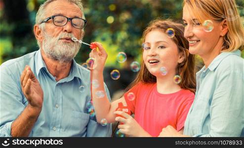 Happy family blows soap bubbles together while going vacation on weekend in the garden park in summer. Kid education and family activities concept.