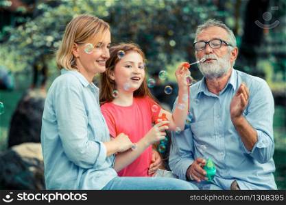 Happy family blows soap bubbles together while going vacation on weekend in the garden park in summer. Kid education and family activities concept.. Happy family blowing soap bubbles in the park.