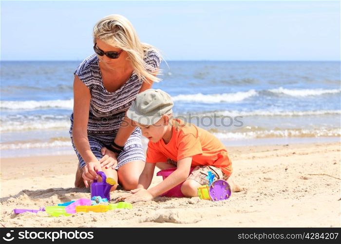 Happy family child son and mother playing toys on beach sea background