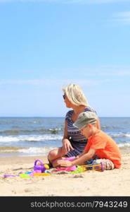 Happy family child son and mother playing toys on beach sea background