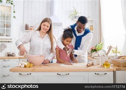 Happy family cooking cakes on breakfast in the kitchen. Mother, father and their daughter prepares the dough in the morning, good relationship. Happy family cooking cakes on breakfast in kitchen