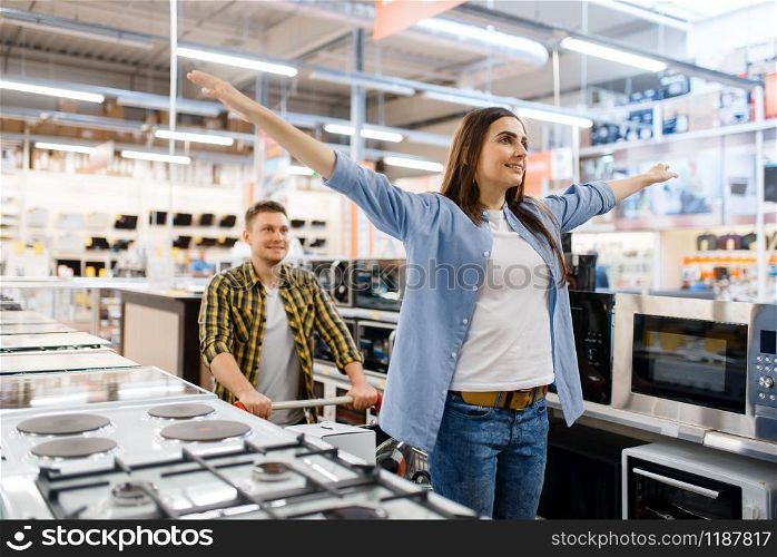 Happy family couple with cart in electronics store. Man and woman buying home electrical appliances in market. Happy family couple in electronics store